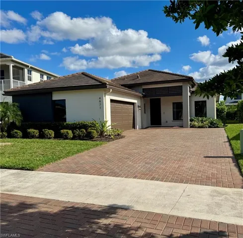 Prairie-style house with decorative driveway, an attached garage, a tile roof, a front lawn, and stucco siding