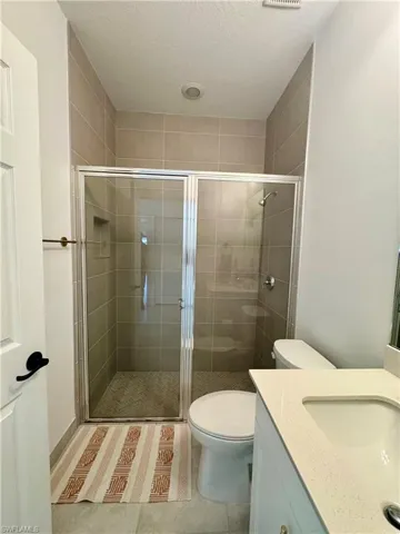 Full bathroom with a textured ceiling, a shower stall, toilet, vanity, and tile patterned flooring