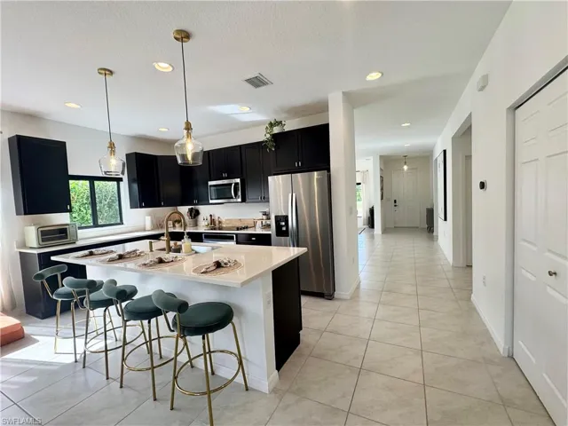 Kitchen featuring light countertops, a breakfast bar area, appliances with stainless steel finishes, visible vents, and dark cabinets