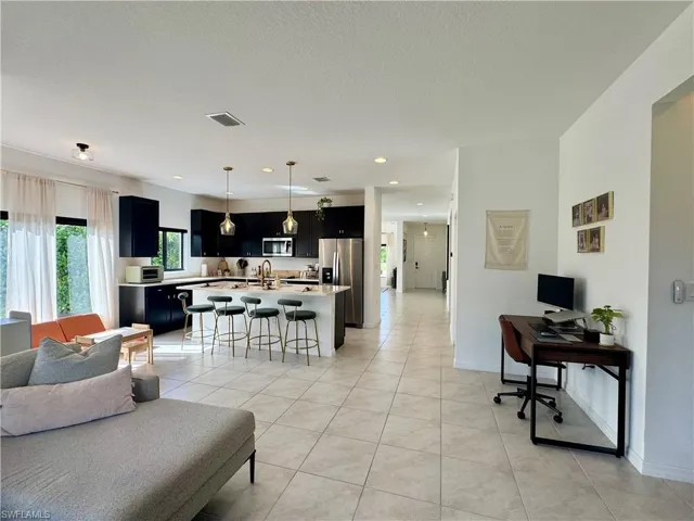 Living area featuring light tile patterned flooring, baseboards, visible vents, and a textured ceiling