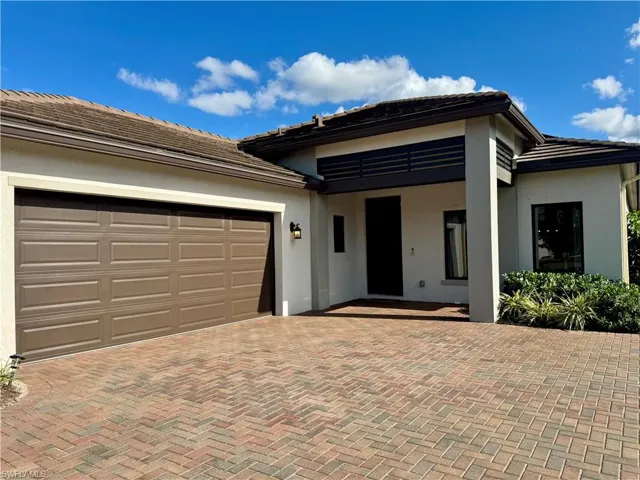 View of front facade with stucco siding, a garage, a tiled roof, and decorative driveway