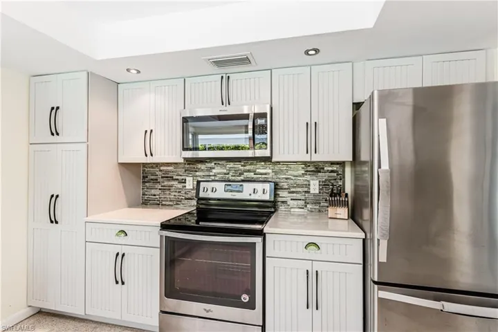 Kitchen with stainless steel appliances, light countertops, backsplash, recessed lighting, and white cabinets