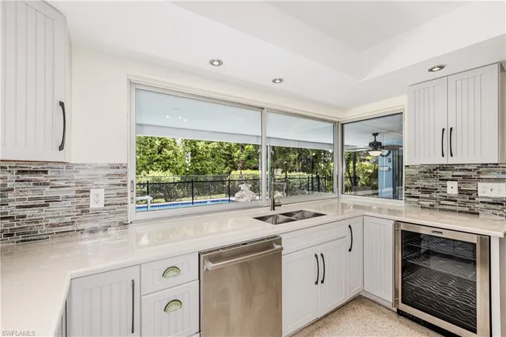Kitchen featuring beverage cooler, stainless steel dishwasher, backsplash, recessed lighting, and white cabinetry