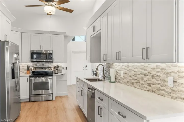 Kitchen with stainless steel appliances, backsplash, white cabinets, light stone countertops, and light wood finished floors