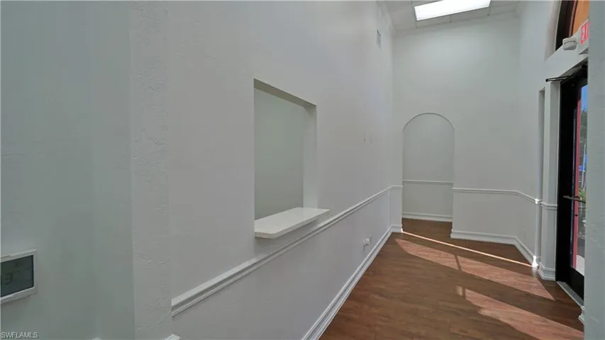 Hall with arched walkways, dark wood-style flooring, a high ceiling, and a textured wall