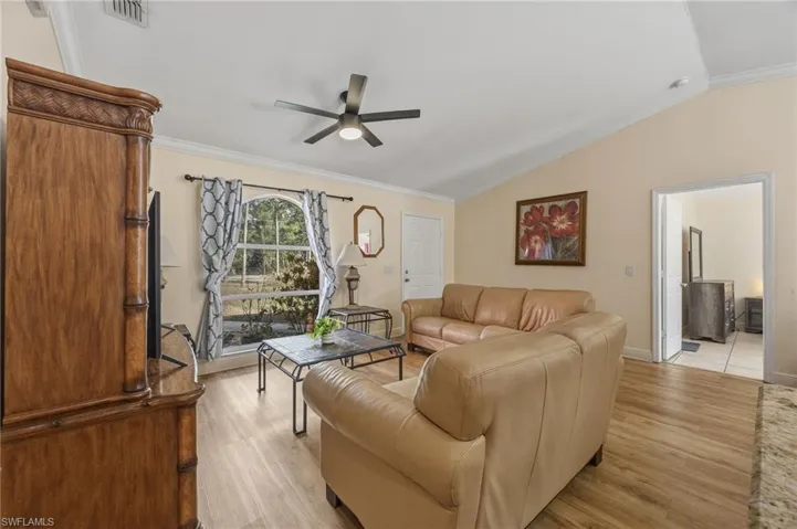 Living room with crown molding, light wood finished floors, a ceiling fan, and lofted ceiling