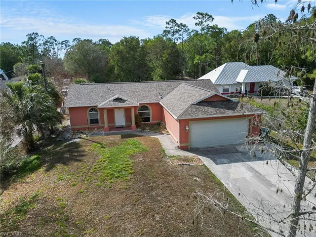 Single story home with a shingled roof, an attached garage, driveway, stucco siding, and view of wooded area