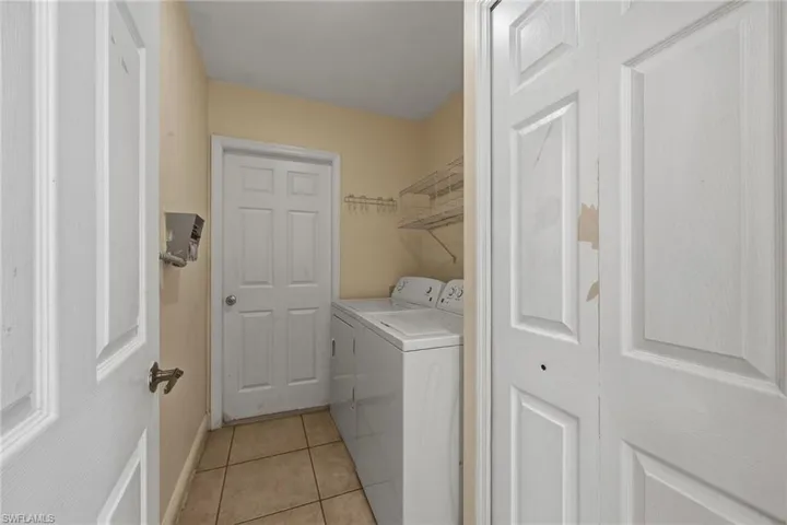 Laundry area with washing machine and clothes dryer and light tile patterned flooring