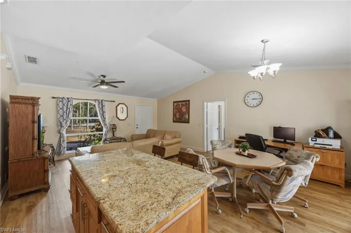 Kitchen with light wood-type flooring, crown molding, light stone countertops, wood finish cabinets, and open floor plan