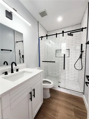 Bathroom with a stall shower, toilet, wood finished floors, a textured ceiling, and vanity