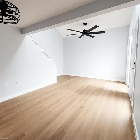 Unfurnished living room with light wood-type flooring, ceiling fan, vaulted ceiling, and baseboards