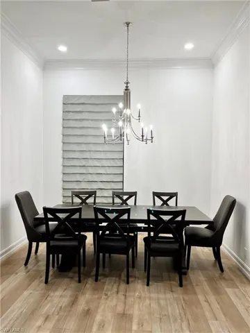 Dining space with light wood-type flooring, crown molding, and an inviting chandelier