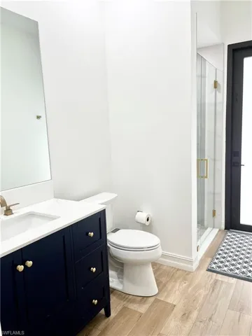 Pool bath with wood-type flooring, vanity, toilet, and a shower with door