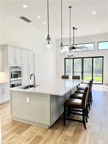 Open Kitchen with sink, light hardwood / wood-style flooring, a large island with sink, pendant lighting, and white cabinets