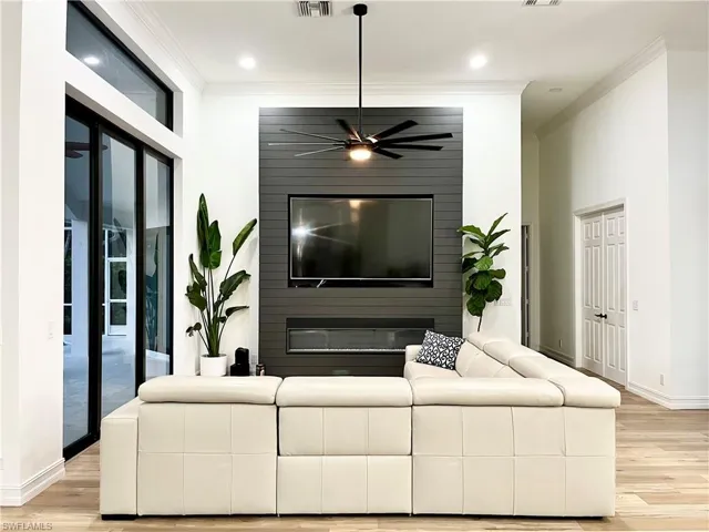 Open Living room featuring a fireplace, light wood-type flooring, ceiling fan, and ornamental molding