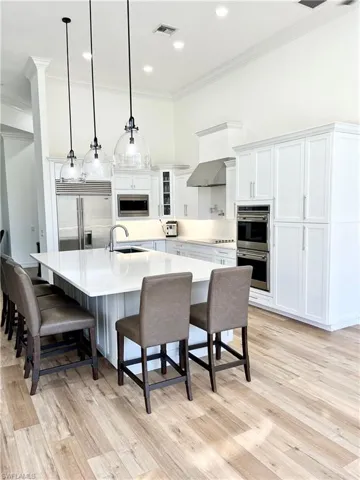 Open Kitchen with a spacious island, sink, built in appliances, white cabinets, and hanging light fixtures