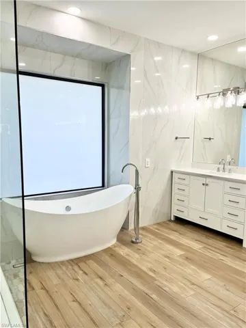 Bathroom featuring hardwood / wood-style flooring, vanity, a bath, and tile walls