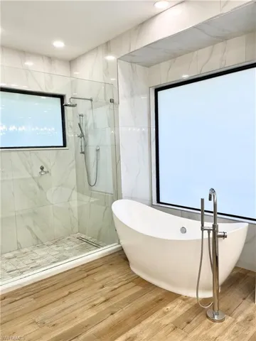 Master Bathroom with hardwood / wood-style floors, separate shower and tub, and a wealth of natural light