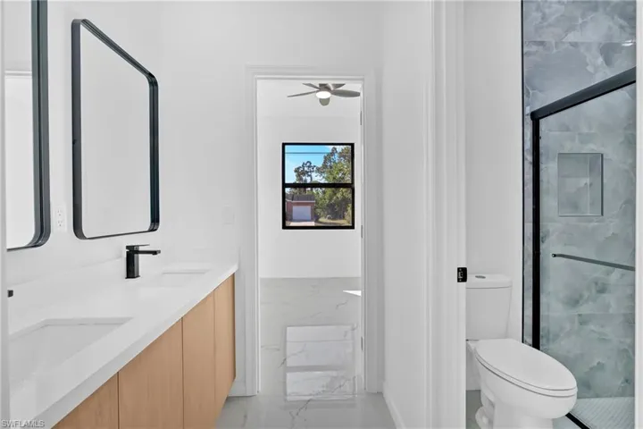 Full bath with a marble finish shower, double vanity, ceiling fan, and light marble finish flooring
