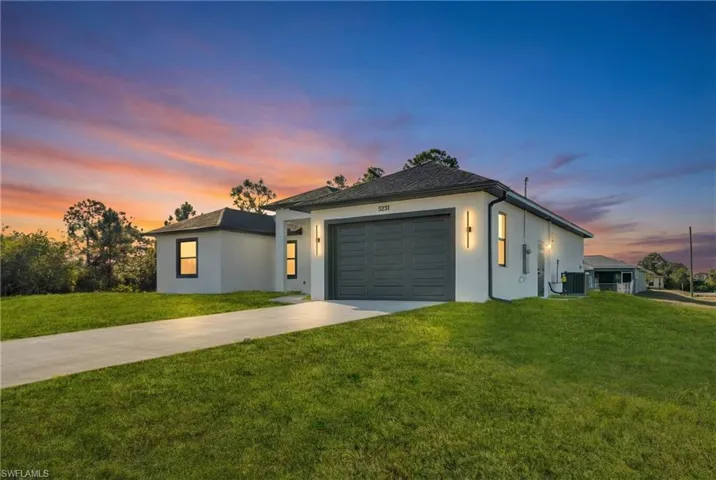 View of front of house featuring concrete driveway, stucco siding, a yard, and a garage