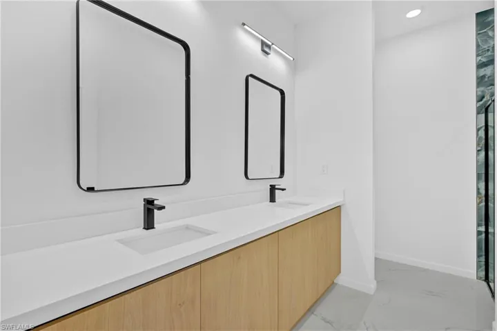 Bathroom featuring double vanity, light marble finish flooring, and recessed lighting