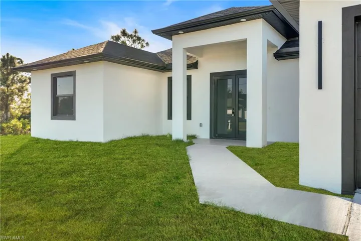 Entrance to property with a yard, stucco siding, roof with shingles, and french doors