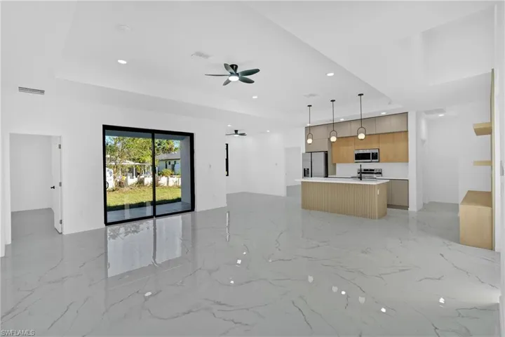 Unfurnished living room with a tray ceiling, ceiling fan, recessed lighting, and light marble finish floors