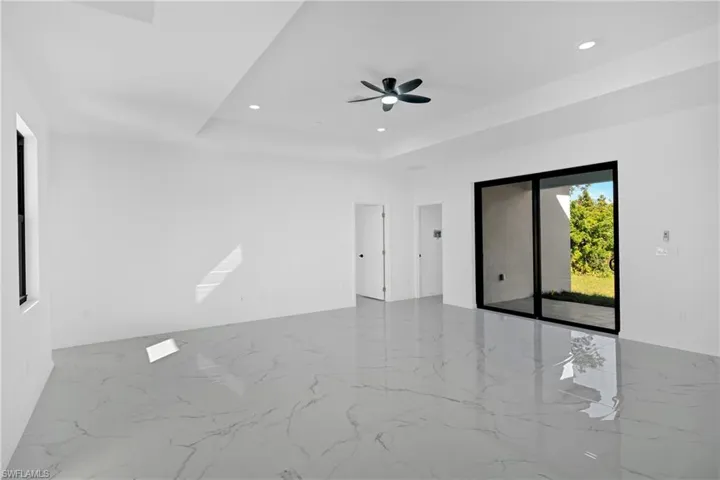 Unfurnished room featuring recessed lighting, light marble finish flooring, ceiling fan, and a tray ceiling