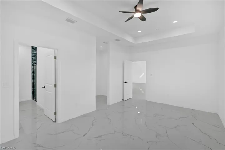 Unfurnished room featuring recessed lighting, a raised ceiling, a ceiling fan, and light marble finish floors
