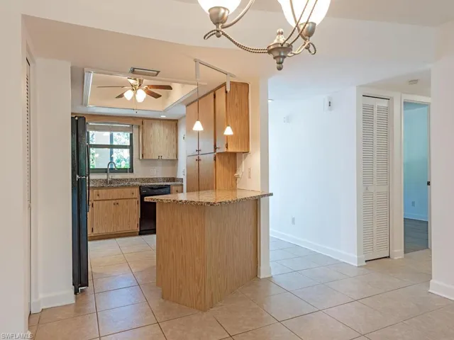 Kitchen featuring hanging light fixtures, a raised ceiling, a peninsula, light stone countertops, and light tile patterned floors