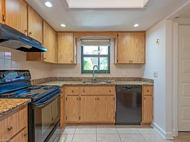 Kitchen with black appliances, decorative backsplash, light stone countertops, and recessed lighting