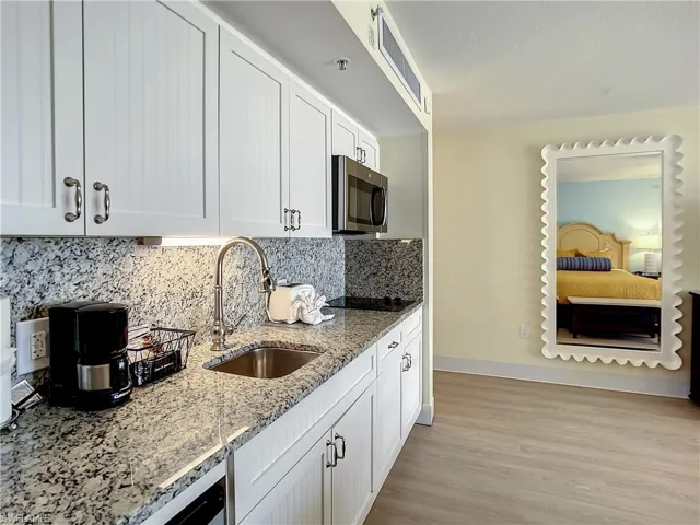Kitchen featuring tasteful backsplash, white cabinets, sink, light stone countertops, and light hardwood / wood-style flooring