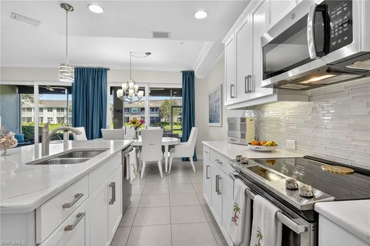 Kitchen featuring appliances with stainless steel finishes, white cabinets, ornamental molding, hanging light fixtures, and backsplash