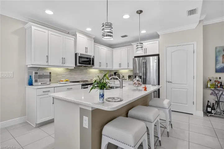 Kitchen featuring tasteful backsplash, stainless steel appliances, a breakfast bar area, light tile patterned floors, and an island with sink