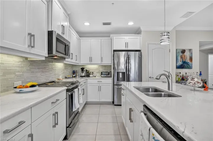 Kitchen featuring appliances with stainless steel finishes, light tile patterned flooring, hanging light fixtures, light stone counters, and tasteful backsplash