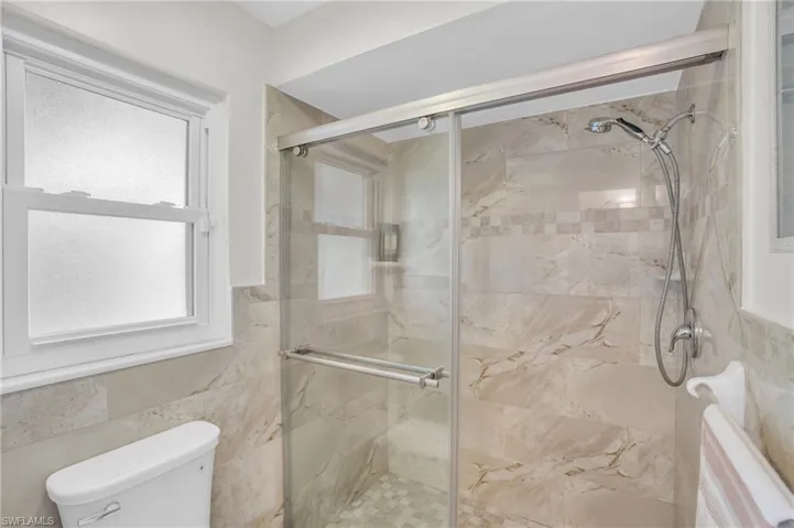 Bathroom with tile walls, a shower with door, and toilet