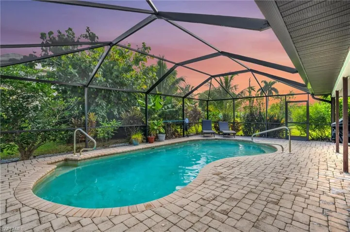 Pool at dusk with glass enclosure and a patio area