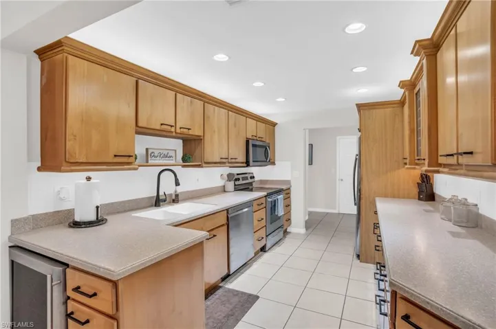 Kitchen featuring beverage cooler, light tile patterned flooring, appliances with stainless steel finishes, and sink