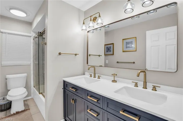 Bathroom with toilet, dual bowl vanity, and tile patterned flooring