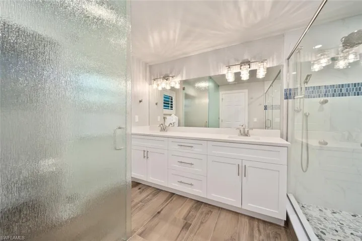 Full bathroom with a stall shower, double vanity, and wood finish floors