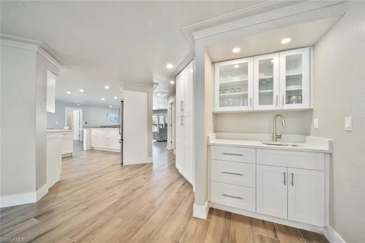 Bar featuring white cabinets, glass insert cabinets, a textured wall, light wood-style flooring, and light stone counters