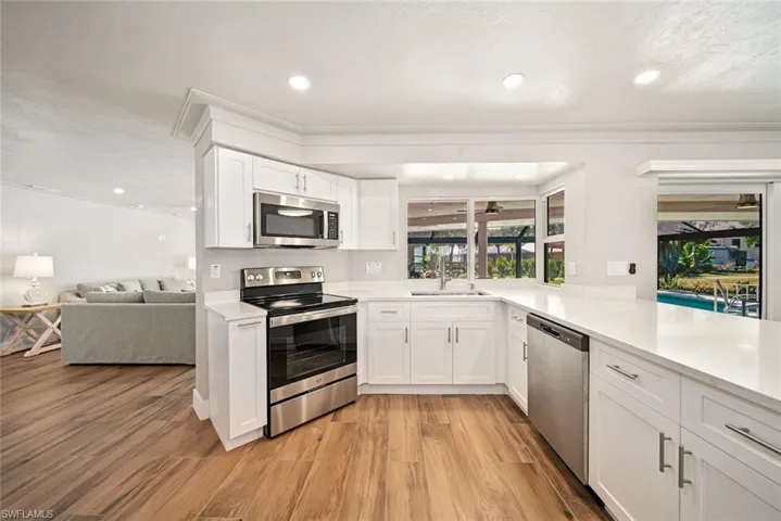 Kitchen featuring stainless steel appliances, white cabinetry, ornamental molding, light wood-style flooring, and recessed lighting