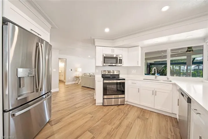 Kitchen with appliances with stainless steel finishes, white cabinetry, ornamental molding, light wood-style floors, and recessed lighting