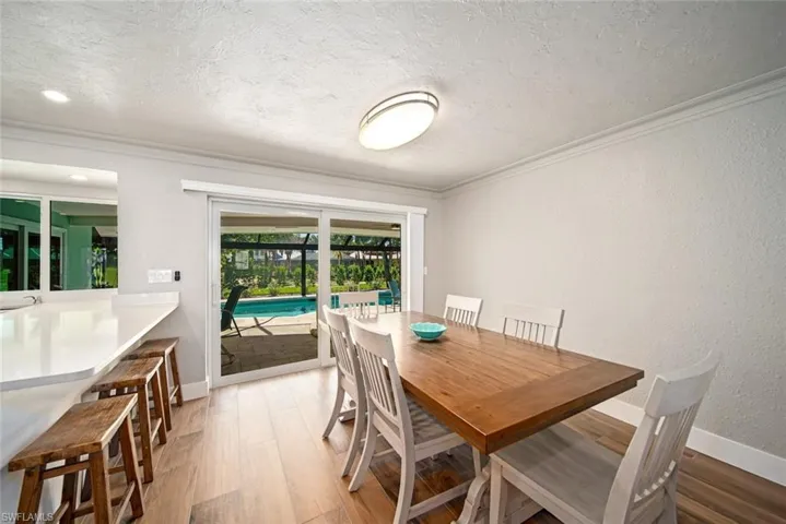 Dining space with a textured ceiling, a textured wall, light wood finished floors, and ornamental molding