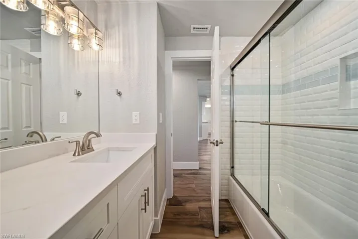 Full bathroom featuring combined bath / shower with glass door, vanity, dark wood-style floors, and a textured wall