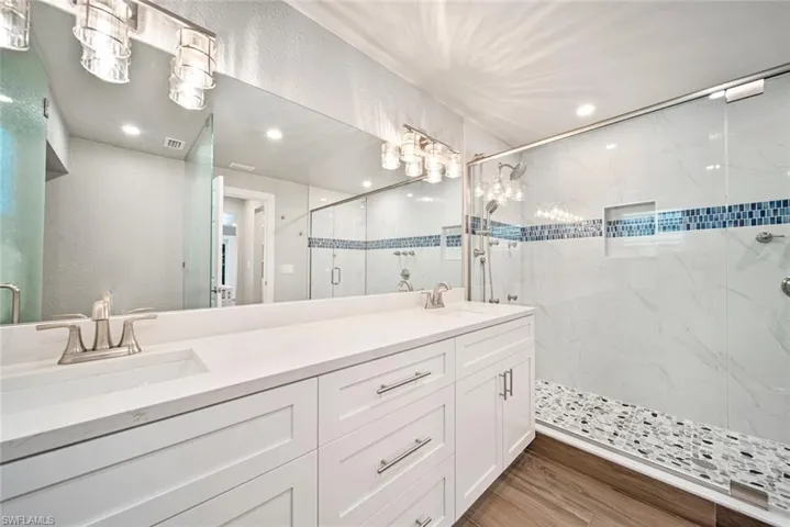 Bathroom featuring a marble finish shower, double vanity, light wood finished floors, recessed lighting, and a textured wall