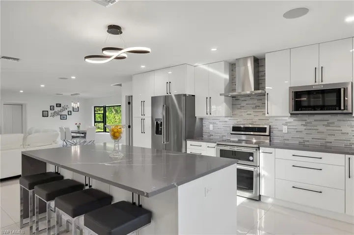 Kitchen with a breakfast bar, stainless steel appliances, wall chimney range hood, white cabinets, and hanging light fixtures