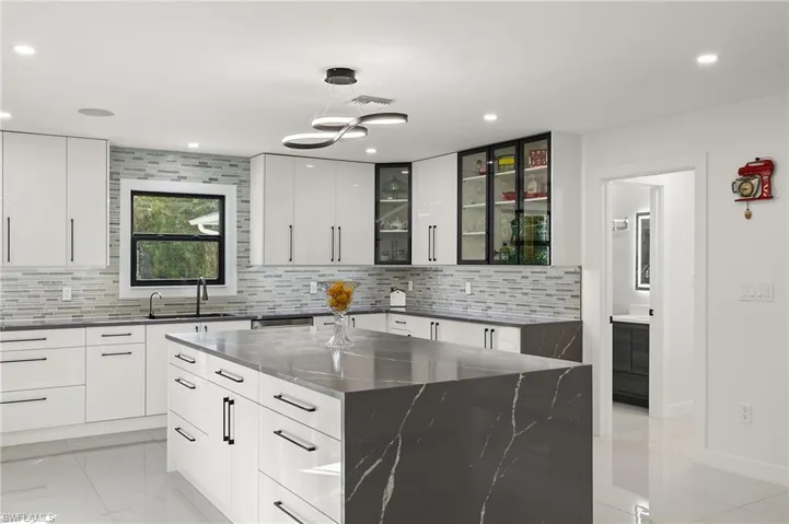 Kitchen with tasteful backsplash, dark stone counters, a spacious island, sink, and white cabinetry