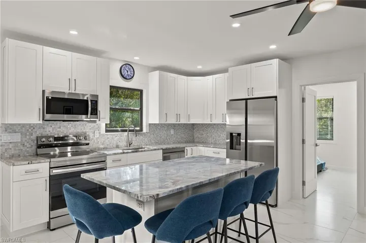 Guest House Kitchen with light stone countertops, a breakfast bar, a kitchen island, and appliances with stainless steel finishes