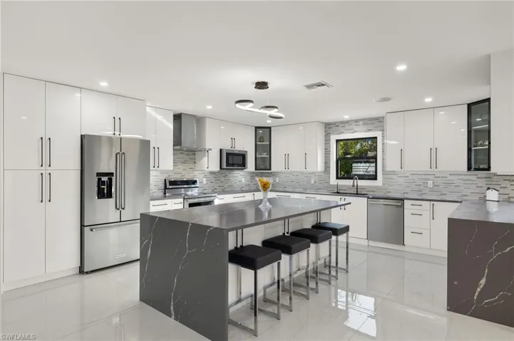 Kitchen featuring appliances with stainless steel finishes, tasteful backsplash, wall chimney range hood, a center island, and white cabinetry